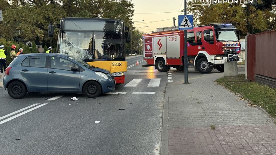 Zderzenie samochodu osobowego z autobusem miejskim na skrzyżowaniu, obok straż pożarna i ekipa ratunkowa.