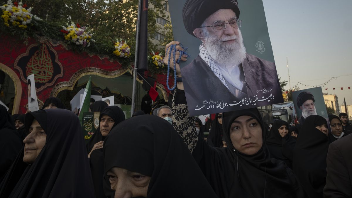 A veiled Iranian woman holds a portrait of Iran's Supreme Leader, Ayatollah Ali Khamenei, while participating in a funeral for unknown martyrs from the Iran-Iraq War (1980-1988) in Tehran, Iran, on November 24, 2025. (Photo by Morteza Nikoubazl/NurPhoto via Getty Images)