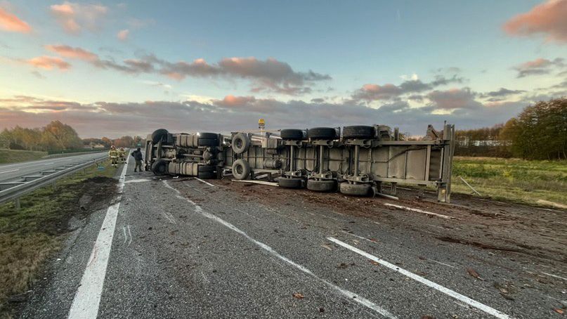 Cysterna leżąca na boku na drodze ekspresowej, obok pracownicy służb ratunkowych zabezpieczający miejsce zdarzenia.
