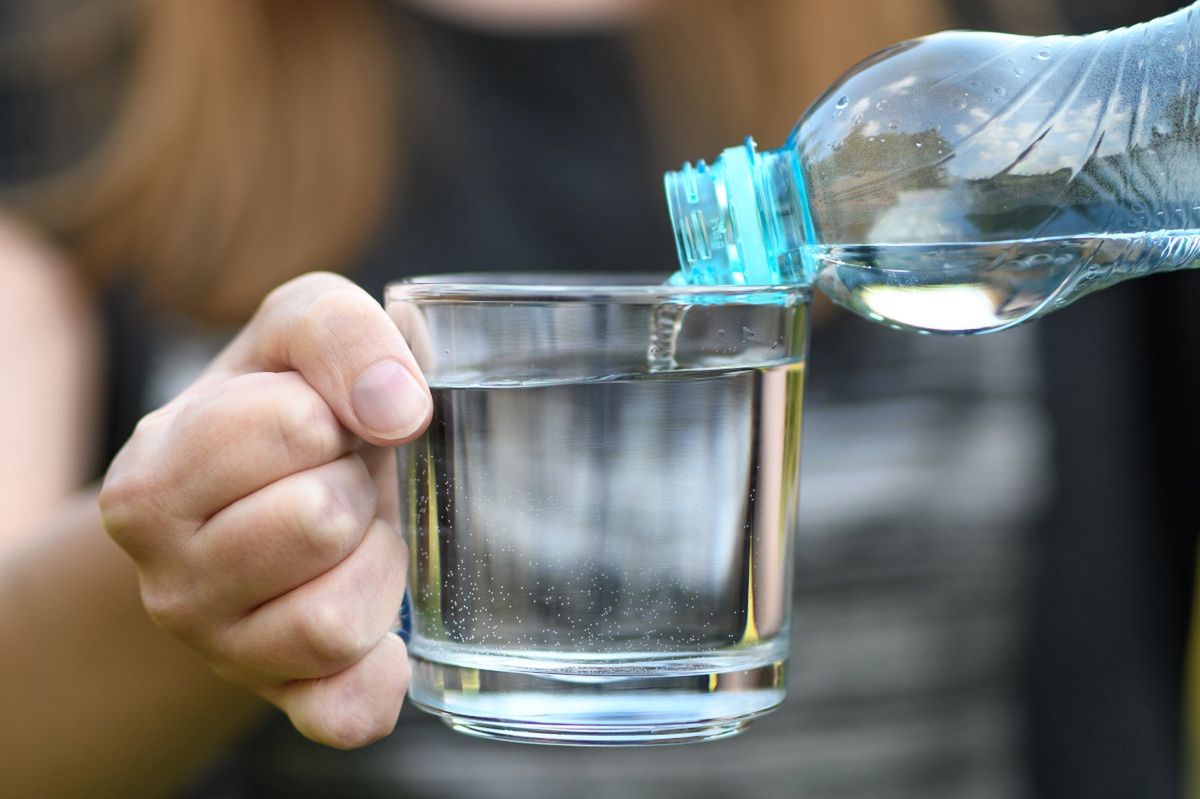 Frau, die Wasser aus einer Flasche in ein Glas gießt