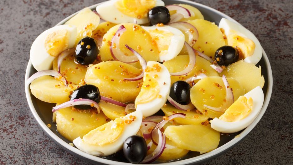 Oriental Romanian potato salad with boiled eggs, onion and olives seasoned with mustard sauce close-up in a plate. horizontal