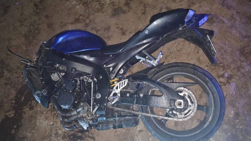 Uszkodzony czarny motocykl leży na ziemi w nieoświetlonym otoczeniu, z widocznymi zarysowaniami i zabrudzeniami.