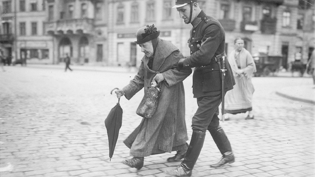 Policjant przeprowadza staruszkę przez ulicę