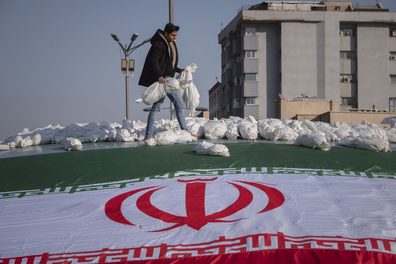 An Iranian man carrying shroud-wrapped packages, symbolizing the bodies of Palestinian children, while walking next to an Iranian flag at Enghelab (Revolution) square during an anti-Israeli rally in Tehran, November 18, 2023. (Photo by Morteza Nikoubazl/NurPhoto via Getty Images)