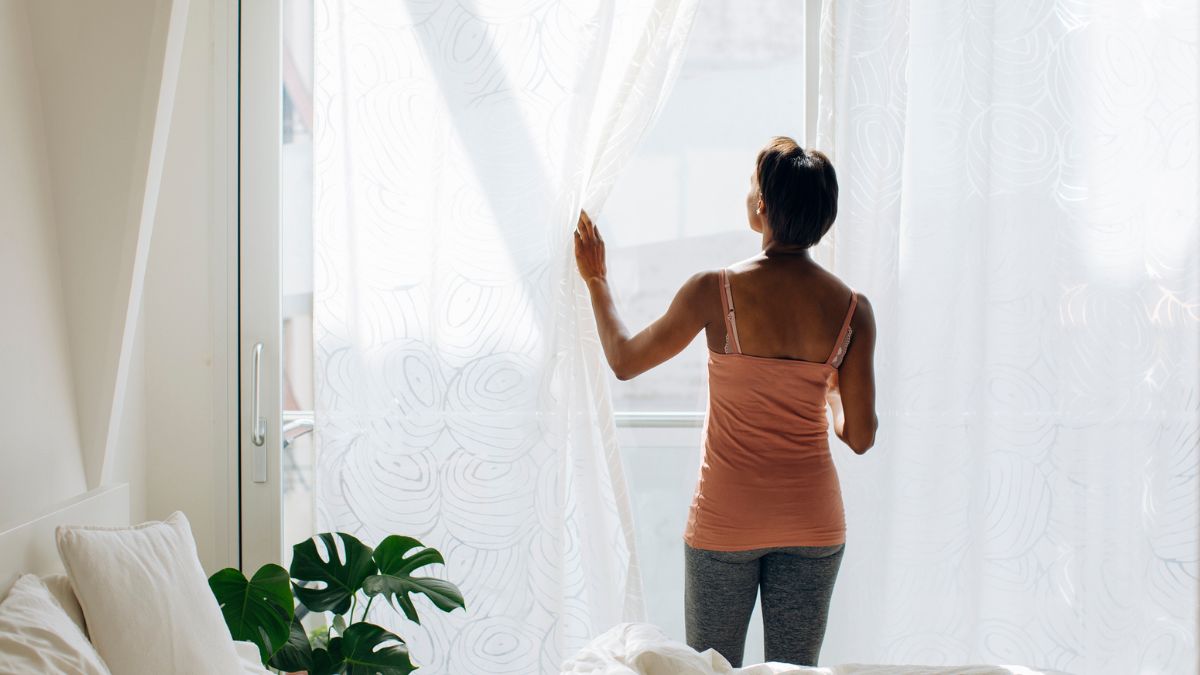 Kobieta odsłania firnaki w oknach.