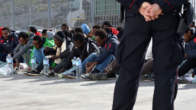 Włoski policjant pilnuje grupy imigrantów; Lampedusa