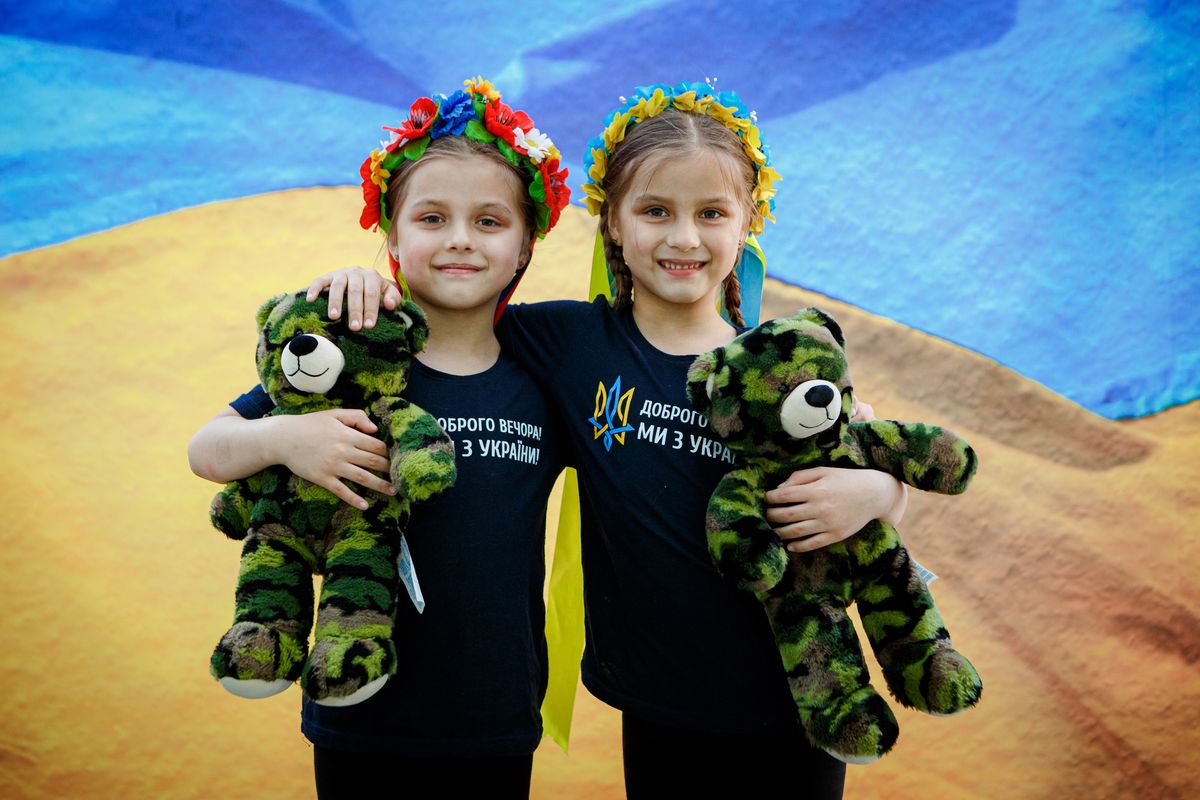 UZHHOROD, UKRAINE - MAY 14, 2022 - Two girls in floral crowns hold camouflage teddy bears as local photographers take the portraits of people against the backdrop of the Ukrainian flag to raise money for the Ukrainian military, Uzhhorod, Zakarpattia Region, western Ukraine. This photo cannot be distributed in the Russian Federation. (Photo credit should read Serhii Hudak/ Ukrinform/Future Publishing via Getty Images)