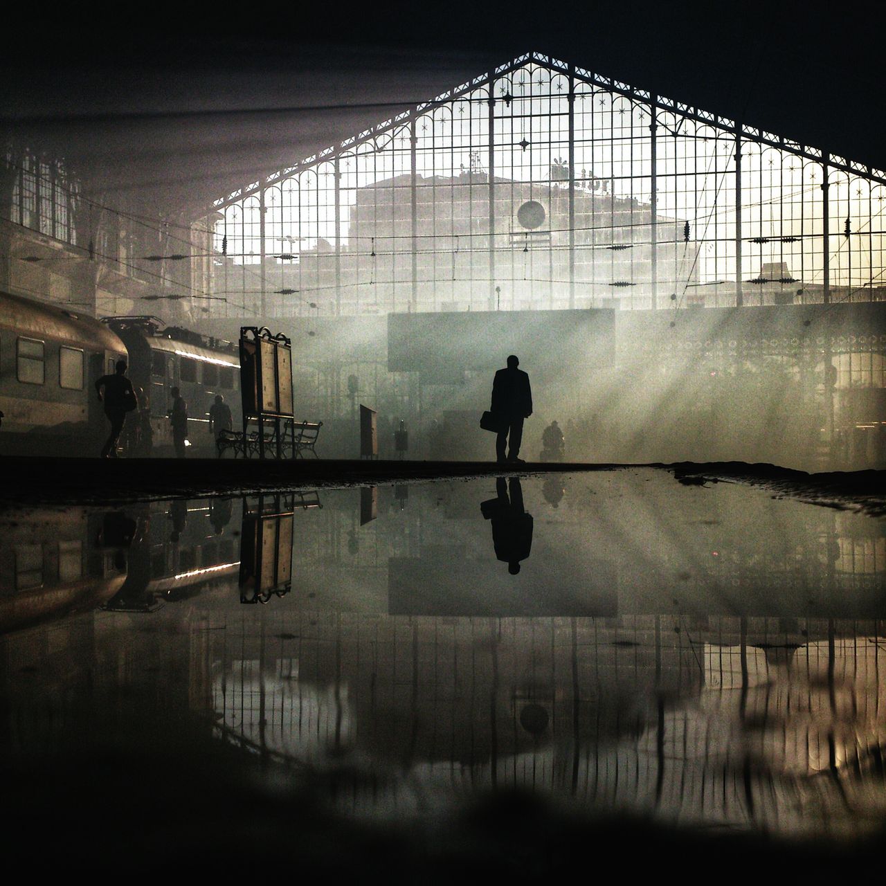 „Nyugati" / „Zachód słońca na dworcu Nyugati w Budapeszcie. Mężczyzna na pustej platformie dworca Nyugati sprawdza rozkład jazdy, tuż po odjeździe pociągu, którym węgierscy kibice jechali na mecz reprezentacji z drużyną Rumunii. Promienie słońca przebijają się przez dym po racach i petardach kibiców" - opisuje historię zdjęcia jego autor Janos M Schmidt.