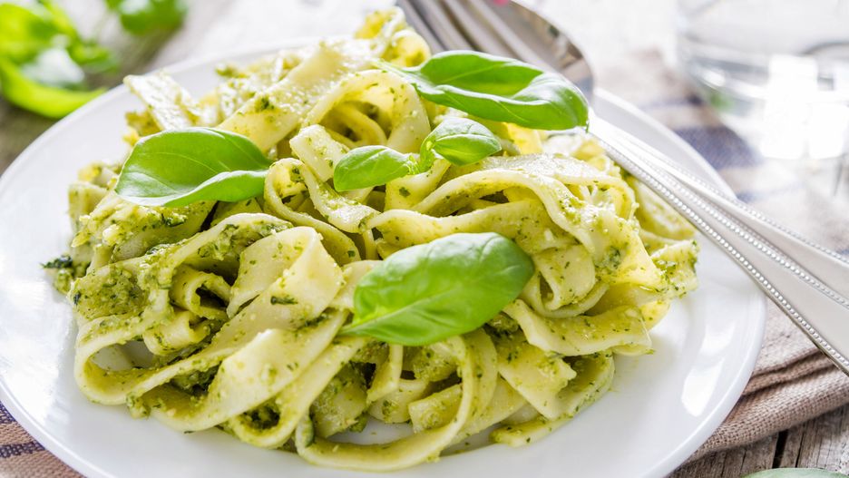 Pesto pasta on white plate, rustic wood background