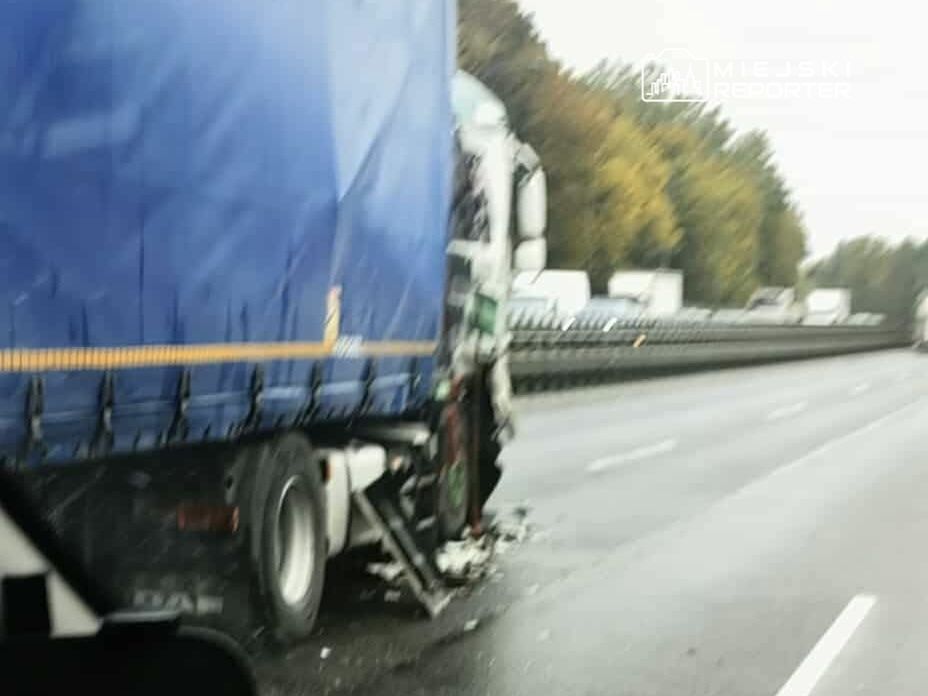 Uszkodzony ciężarówka z niebieską plandeką stoi na autostradzie, w tle widoczne inne pojazdy.