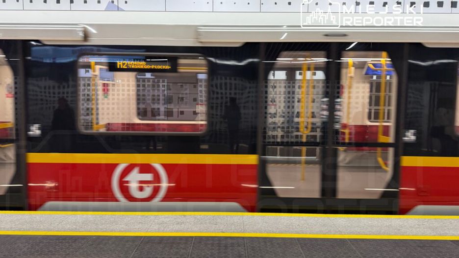 Pociąg metra z wyświetlaczem kierunku "M2 Bemowo" przejeżdża obok peronu w nowoczesnej stacji.