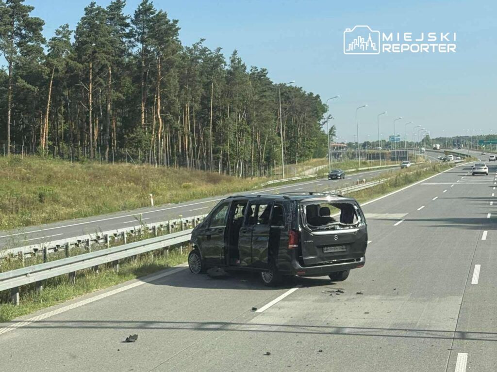 Czarny van z uszkodzoną karoserią stoi na pasie ruchu, obok lasu, z odłamkami na drodze.