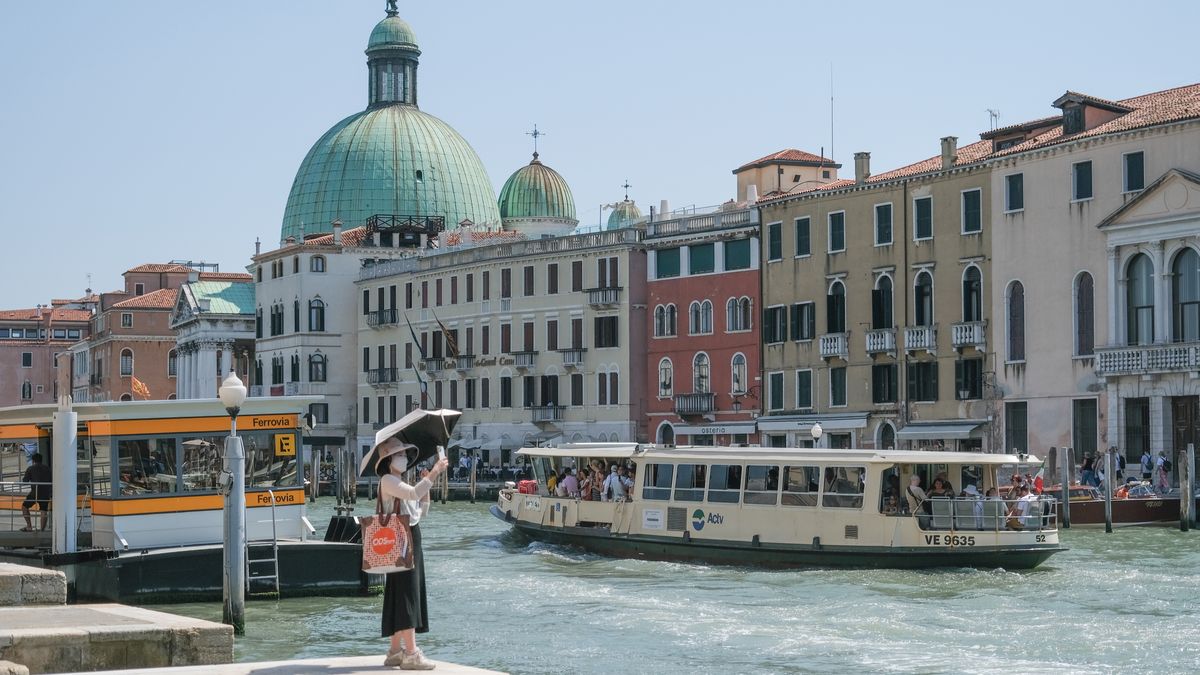 VENICE, ITALY - JULY 04: Tourist shields himself from the sun with an umbrella while taking a photo near the Grand Canal on July 04, 2025 in Venice, Italy. Italy has issued 18 red alerts for hot weather during the current heatwave sweeping Europe. Four people have died and measures have been put in place to limit outdoor working during the hottest part of the day. (Photo by Stefano Mazzola/Getty Images)