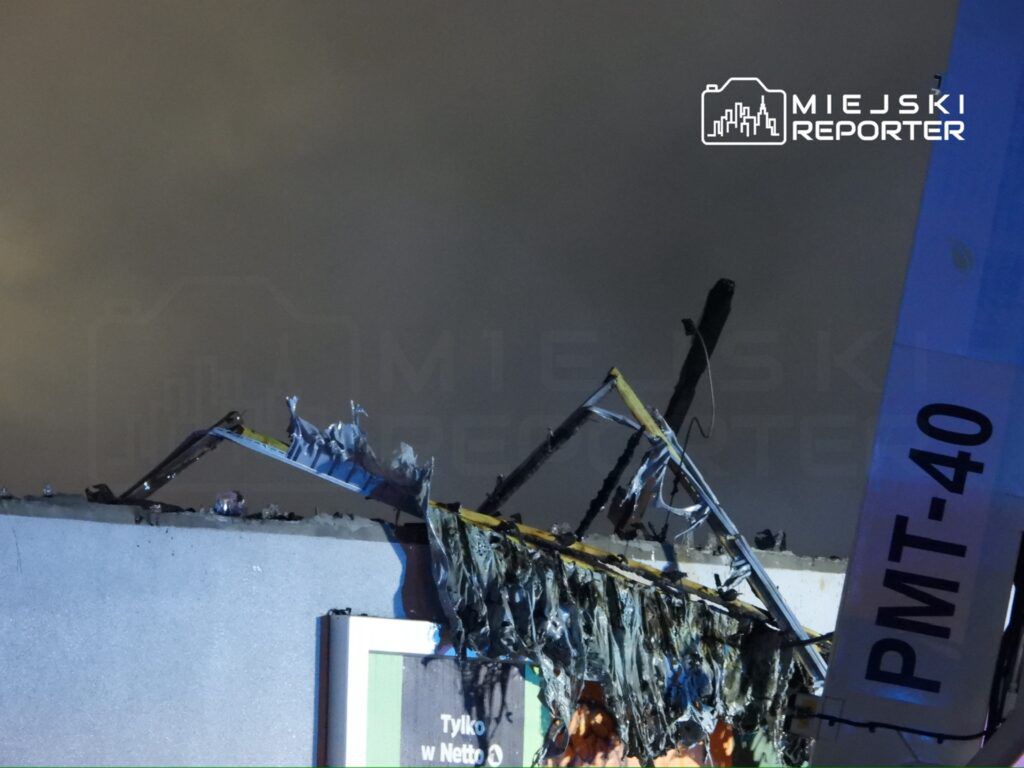 Zniszczony fragment dachu budynku z uszkodzoną konstrukcją, w tle ciemne niebo.