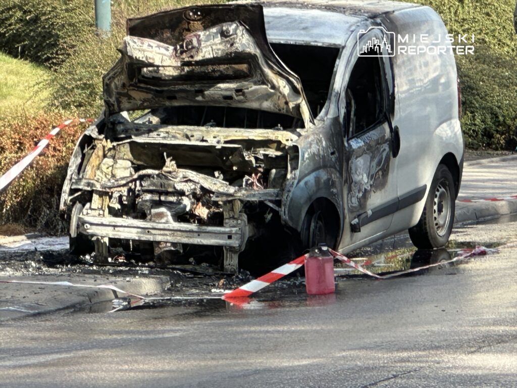 Spalony samochód dostawczy na poboczu drogi, otoczony taśmą ostrzegawczą i pojemnikiem z paliwem.