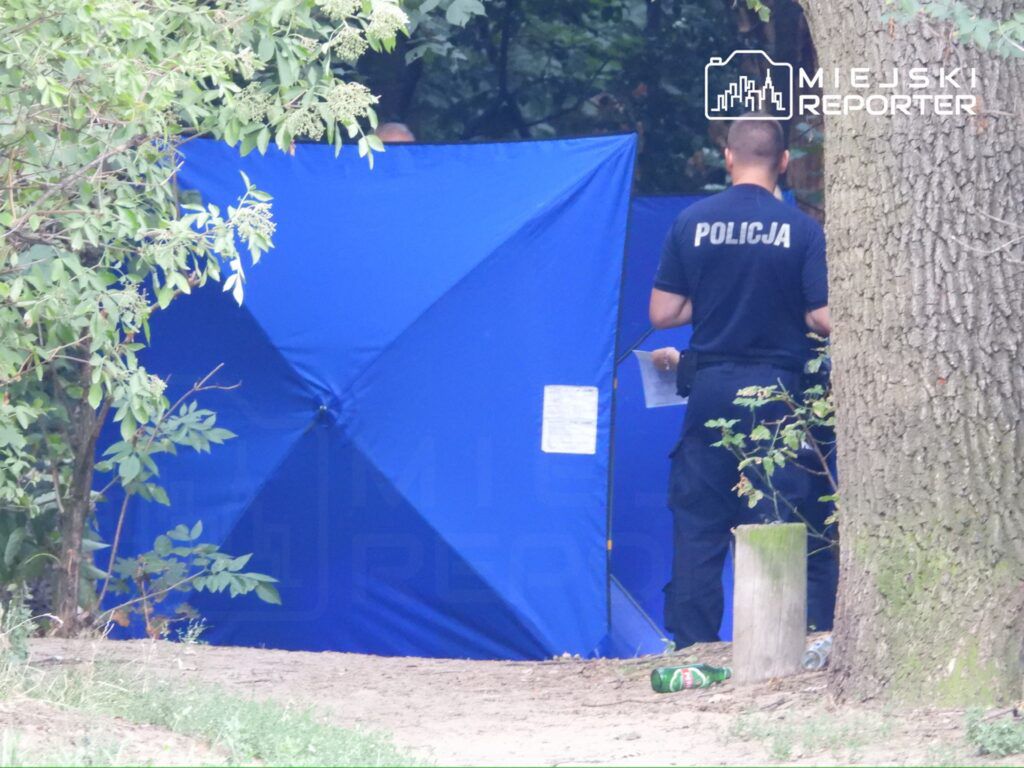 Policjant w mundurze przeszukuje teren w pobliżu niebieskiego namiotu w lesie.