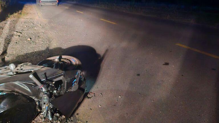 W nocy na drodze leży przewrócony motocykl obok radiowozu policyjnego. Otoczenie jest słabo oświetlone.