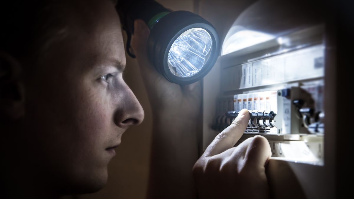 Mężczyzna z latarką sprawdza bezpeczniki