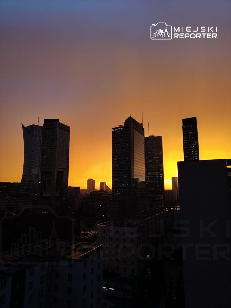 Wysokie wieżowce odbijają pomarańczowe światło zachodzącego słońca w miejskim krajobrazie.