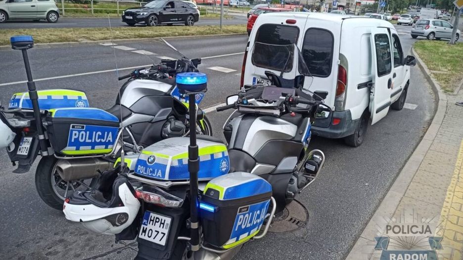 Motocykle policyjne zatrzymane obok białego dostawczego samochodu na ruchliwej ulicy w mieście.