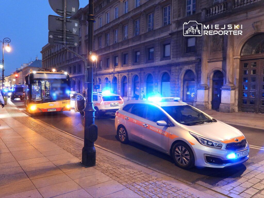 Autobus miejski zatrzymany na ulicy, obok pojazdy służb ratunkowych z włączonymi sygnałami świetlnymi.