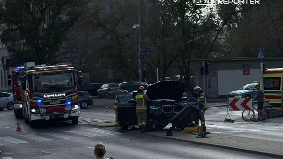 Strażacy pracują nad usunięciem uszkodzonego samochodu na skrzyżowaniu ulicy, obok stojącego wozu strażackiego.