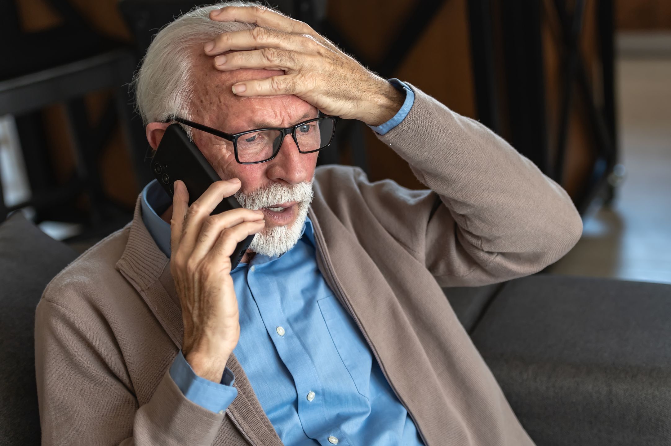 elderly, senior, old man, worried, stressed, phone call, emergency, concern, anxiety, problem, bad news, reaction, facial expression, home, indoor, glasses, beard, cardigan, blue shirt, distress, communication, mobile phone, talking, shocked, surprised, serious, elderly care, healthcare, crisis, fear, emotions, loneliness, retirement, aging, mature adult, senior citizen, thinking, decision-making, financial issues, scam, fraud, technology, worried expression, home interior, close-up, stressful situation, bad news reaction, confused, uncertainty