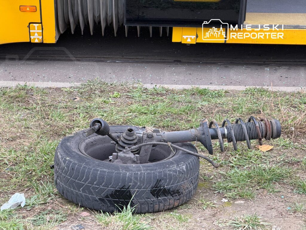 Zdemontowane zawieszenie z oponą leży na trawie obok przystanku autobusowego.