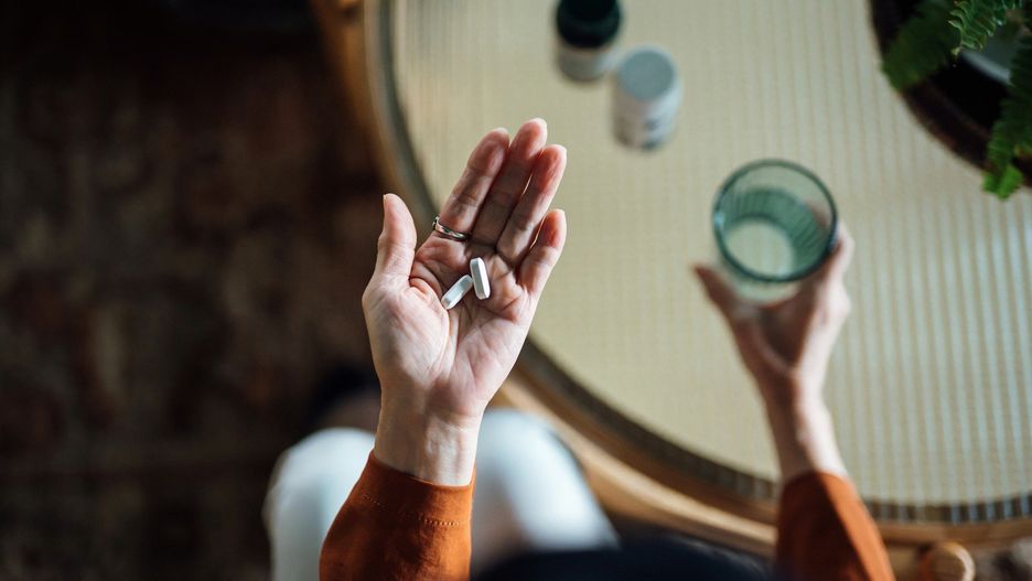 Overhead view of senior Asian woman feeling sick, taking medicines in hand with a glass of water at home. Elderly and healthcare concept