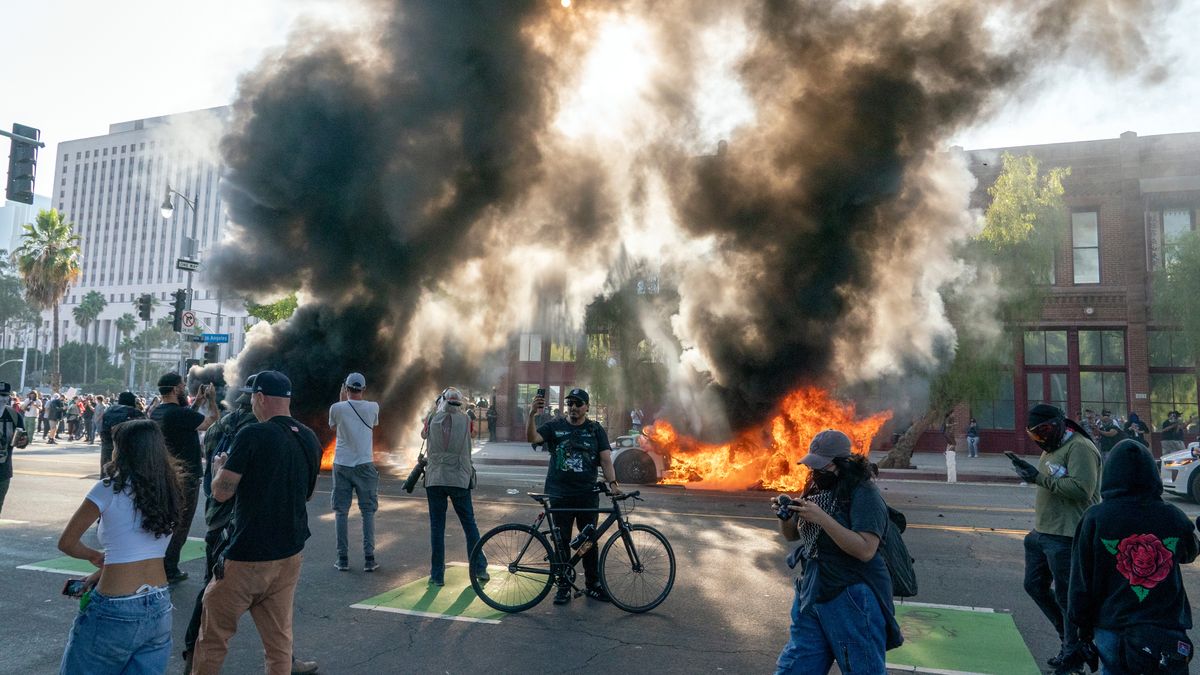 Cars burn behind protesters during a demonstration in Los Angeles, California, US, on Sunday, June 8, 2025. Tensions flared during a demonstration in Los Angeles on the third day of anti-deportation protests, as demonstrators clashed with law enforcement while President Donald Trump and California Governor Gavin Newsom exchanged blame over the unrest and responsibility for restoring order. Photographer: Kyle Grillot/Bloomberg via Getty Images