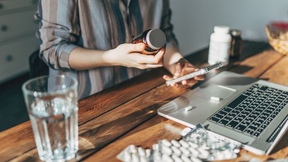 Mature Woman with blister pack of pills and smartphone in hand using online pharmacy store, buying pharmacy on internet, ordering medicine online at home.