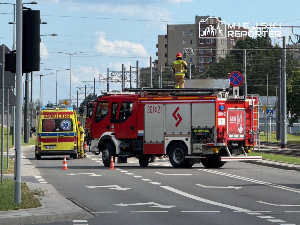 Zespół ratunkowy w żółtej karetce współpracuje z strażakami przy czerwonym wozie strażackim na ulicy.