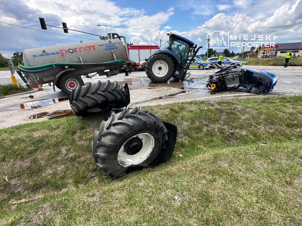 Zniszczony traktor leży na boku obok drogi, a w tle widoczny jest drugi traktor oraz pojazdy policyjne.