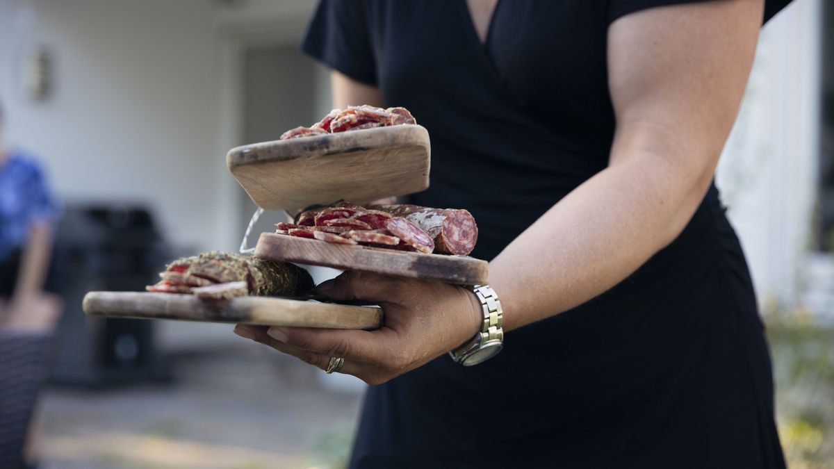 Midesction of woman balancing three serving boards filled with sliced salami
Elva Etienne