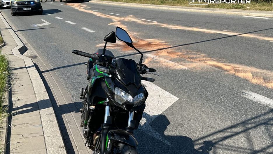 Motocykl stoi na poboczu drogi, obok widać karetki i służby ratunkowe, a na jezdni widoczne są plamy.