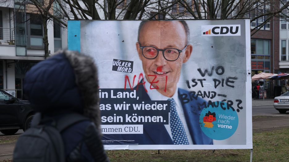 BERLIN, GERMANY - FEBRUARY 05: A woman walks past an election campaign billboard that shows chancellor candidate Friedrich Merz of the German Christian Democrats (CDU/CSU) with graffiti that reads: "Nazi" and "Where is the firewall?" on February 5, 2025 in Berlin, Germany. Merz caused a nationwide uproar recently by seeking to push through new legislation in the Bundestag on immigration with the help of the far-right Alternative for Germany (AfD), thereby breaking the political tabu or "firewall" on collusion with far-right parties. Germany is scheduled to hold snap parliamentary elections on February 23 following the collapse of the three-party federal government coalition last November. (Photo by Sean Gallup/Getty Images)