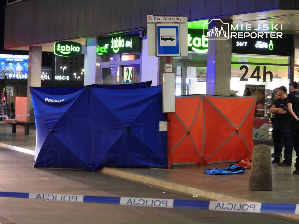 Policjanci zabezpieczają miejsce zdarzenia przy sklepie Żabka, otoczone niebieskimi i pomarańczowymi namiotami.