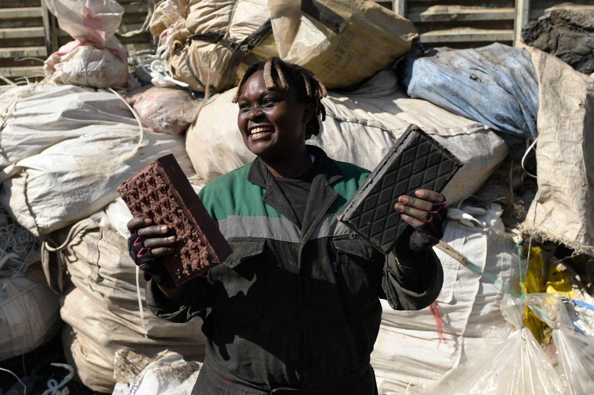 arch44TOPSHOT - Kenyan Nzambi Matee, 29-year-old entrepreneur and inventor, pose as she holds recycled paving bricks, made from plastic wastes in industrial area in Nairobi February 16, 2021. - The plastic waste is initially mixed with sand in a machine at extremely hot temperatures, as it acts as a binder. Then the blended paste is compressed in the next machine into its brick form. Nzambi is the founder of Gjenge(build yourself-in Kiswahili) makers ltd, that recycles plastic waste into bricks that are stronger than concrete,her company initiated following the development of a prototype machine that turns discarded plastic into paving stones. (Photo by Simon MAINA / AFP)SIMON MAINA