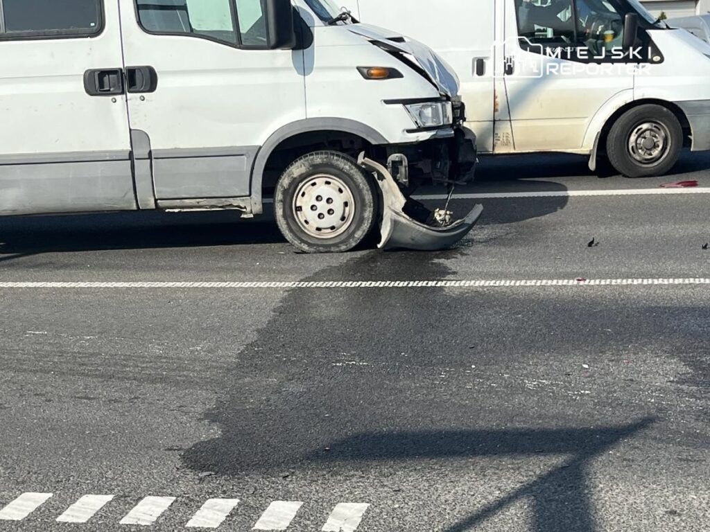 Uszkodzony pojazd dostawczy z usuniętym przednim zderzakiem na drodze, obok innych samochodów.