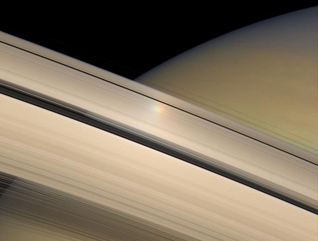 To zdjęcie powstało, gdy Słońce znajdowało się bezpośrednio za sondą. Kolorowa poświata, którą widzicie, to skutek odbicia się światła od pierścienia Saturna. Jest to artefakt związany z rejestrowaniem obrazu podczas poruszania się sondy. Cassini rejestruje obrazy za pomocą nakładania na siebie 3 osobno zapisanych zdjęć z kanałów RGB. 12 lipca 2007 r.