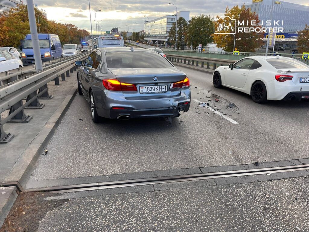 Zderzenie dwóch samochodów na ruchliwej drodze, z uszkodzeniami widocznymi na tylnym zderzaku szarego BMW.