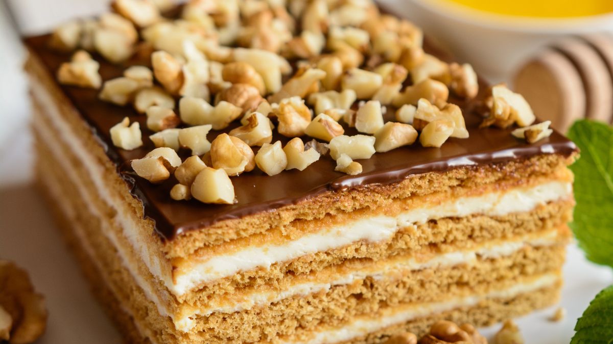 Wiele osób polewa miodownik czekoladą i posypuje orzechami