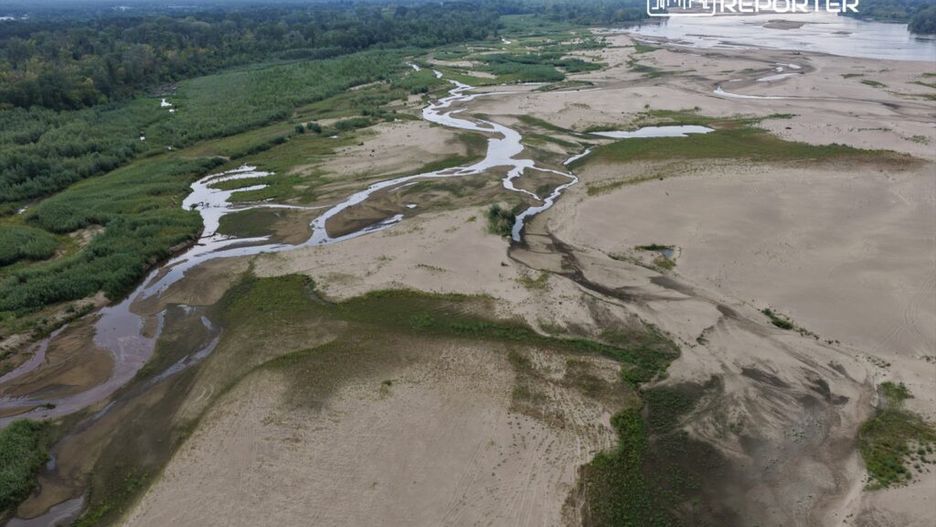 Szeroka panorama piaszczystego terenu z wijącymi się strumieniami i zielonymi zaroślami w tle.