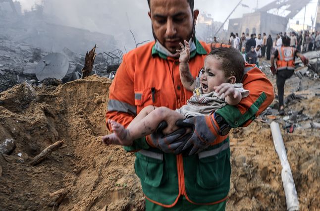 A Palestinian carries a child injured in a rocket attack on Gaza City, October 25