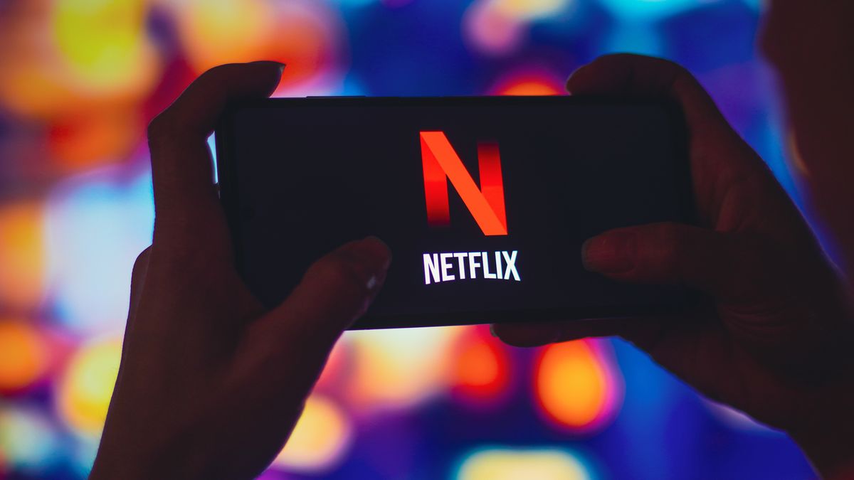 In this photo illustration, a silhouetted woman holds aBRAZIL - 2022/07/06: In this photo illustration, a silhouetted woman holds a smartphone with the Netflix logo displayed on the screen. (Photo Illustration by Rafael Henrique/SOPA Images/LightRocket via Getty Images)SOPA Imageslogos, brand, online, smartphone, cellphone, phone, device