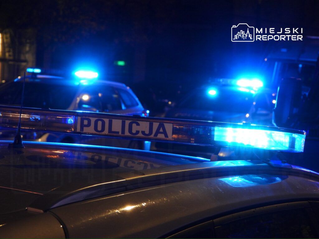 Niebieskie światła policyjnych radiowozów migają w nocy na ulicy, oświetlając otoczenie.