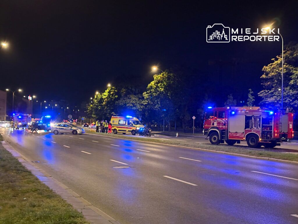 Na drodze w nocy pojazdy ratunkowe, w tym karetki i wóz strażacki, interweniują przy wypadku.
