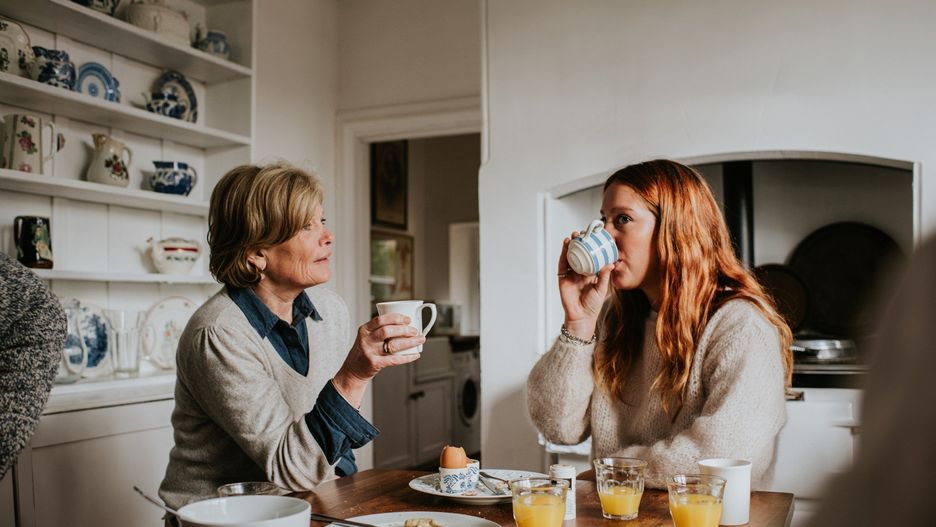 A mother and adult daughter drinking coffee in a stylish kitchen