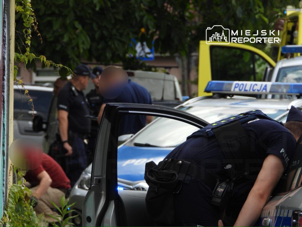 Grupa policjantów prowadzi działania interwencyjne w pobliżu zaparkowanych radiowozów.
