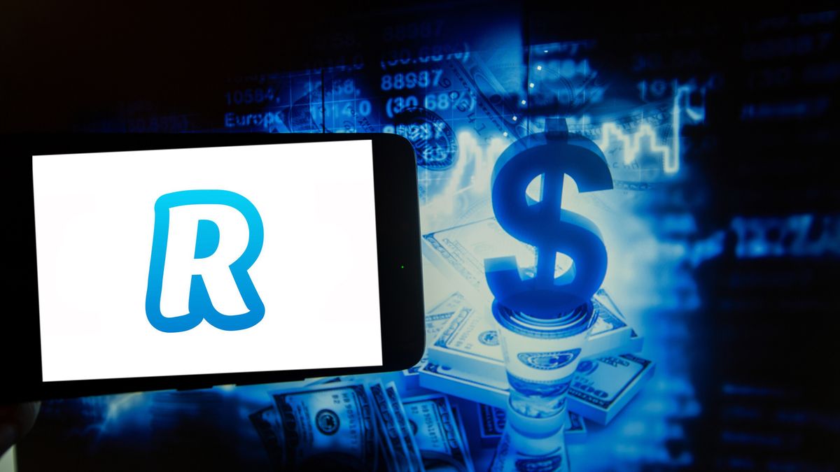 The logo of Revolut is seen on a screen of a smartphone next to an illustration of money and stock market. (Photo illustration by Alexander Pohl/NurPhoto via Getty Images)